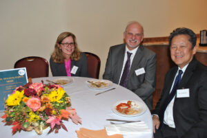 Three people sitting around dining table, smiling.